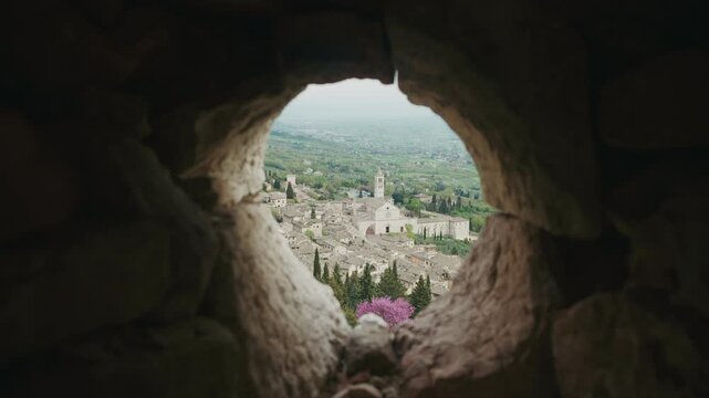 A hole in a rocky wall showing the city of Assisi. Assisi, Italy.