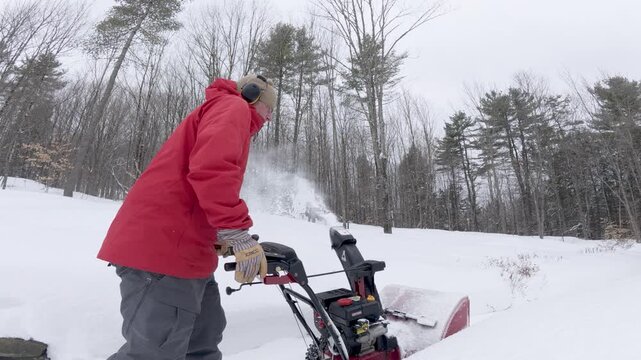 4K video of a man using a snowblower on a snowy driveway in a cold winter snow storm in Quechee, Vermont, New England, USA.