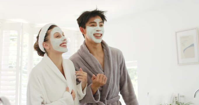 Diverse couple in twenties standing in bathroom wearing robes and masks, tracking offcamera cue