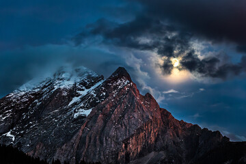 Mountain peak illuminated by moonlight at night. View from the village Canazei, Dolomites, Italy.