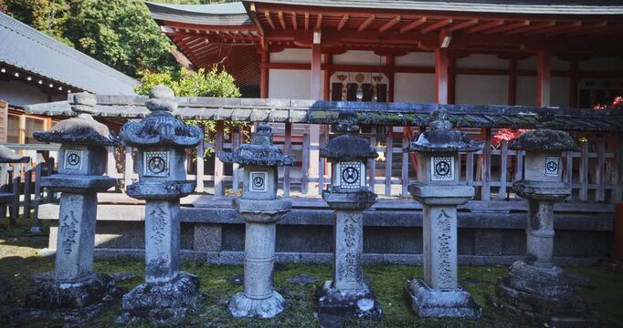 Line of ancient, old stone lanterns in front of ancient Japanese structures - steady cam shot