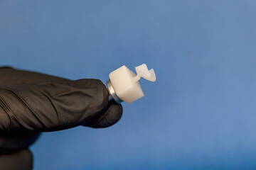 Freshly milled ceramic veneer attached to CAD CAM block held by dentist in black glove. Precision aesthetic dentistry and modern prosthetic workflow concept. © Tatiana