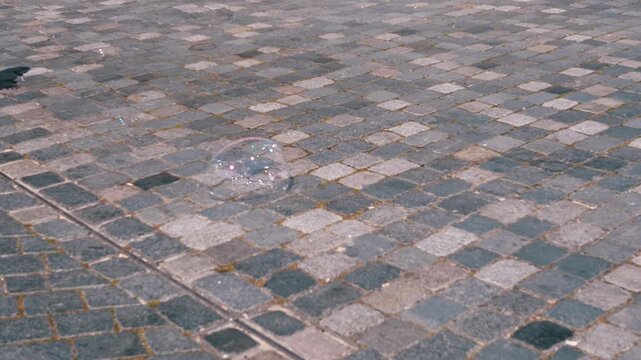 A large soap bubble bounces and rolls across a cobblestone pavement. A simple, playful scene ideal for children's videos or whimsical projects.