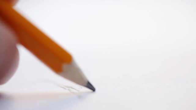 Draws with a pencil on a white sheet of paper in macro view