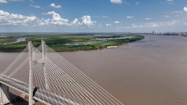 Aerial view crane down with pan and pull back from Rosario-Victoria suspension bridge toward Parana River in Argentina. Drone shot revealing crossing, waterway and cargo barges