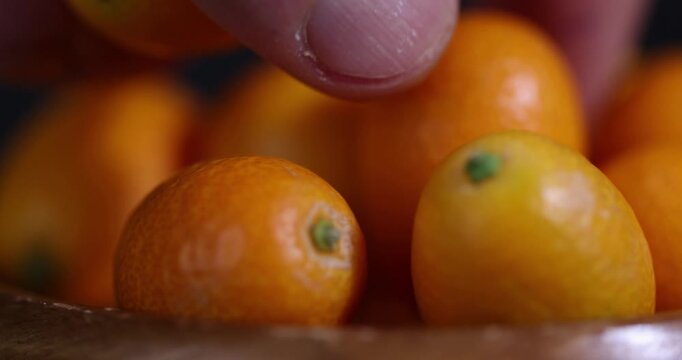 small orange fruits of juicy fresh and fragrant kumquat on a wooden table, oval oblong kumquat fruit scattered on a black table made of pine wood
