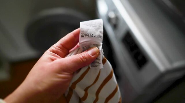 Woman reading clothing label with care symbols and information on clothing near washing machine, closeup