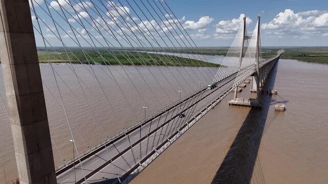 Aerial view pushing in diagonally toward Rosario-Victoria suspension bridge with traffic in Argentina. Drone shot revealing crossing over Parana River