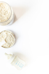 Baby milk bottle and powdered infant formula in the jar and scoop on white background. Top view.