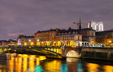 Fototapeta premium Pont Notre-Dame bridge spans the Seine river leading to the illuminated Hotel-Dieu hospital and Notre-Dame Cathedral under reconstruction at night in Paris, France