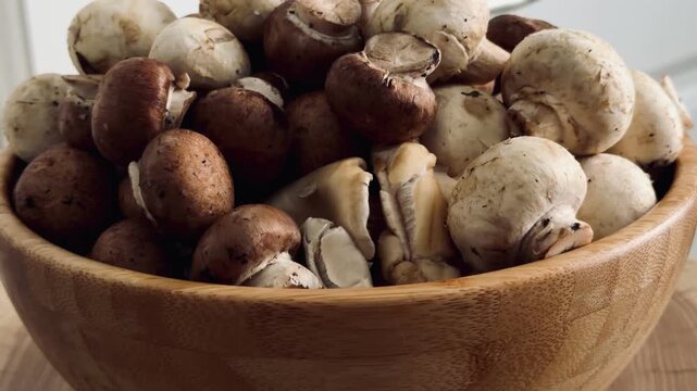 Fresh white button mushrooms and brown champignons in a wooden bowl on a natural oak slab. Rustic close-up of organic edible fungi, perfect for healthy cooking and farmhouse kitchen decor.