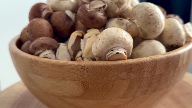 Fresh white button mushrooms and brown champignons in a wooden bowl on a natural oak slab. Rustic close-up of organic edible fungi, perfect for healthy cooking and farmhouse kitchen decor.