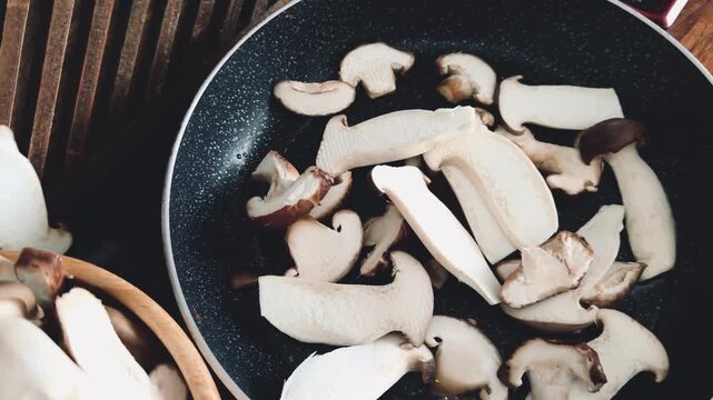 Close-up of hand throwing assorted sliced mushrooms into a hot frying pan. Preparation of gourmet shiitake, shimeji, and king oyster mushrooms for a healthy vegan meal. Motion blur, cooking process.
