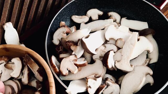 Close-up of hand throwing assorted sliced mushrooms into a hot frying pan. Preparation of gourmet shiitake, shimeji, and king oyster mushrooms for a healthy vegan meal. Motion blur, cooking process.