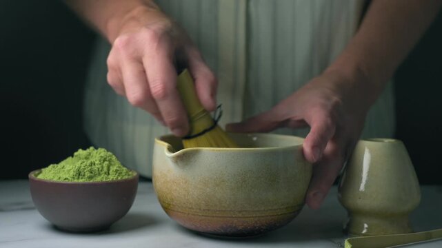 A woman whisking matcha with a bamboo whisk, preparing a healthy drink from traditional Japanese green tea.