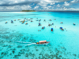 Aerial view of colorful boats and yachts in transparent water on sunny summer day. Mnemba island, Zanzibar. Top view of sandbank in low tide, blue sea, turquoise water, yachts, sky with clouds. Ocean © den-belitsky