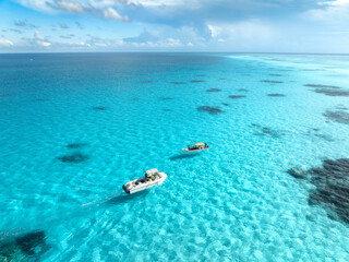 Obraz premium Aerial view of colorful boats and yachts in clear water on sunny summer day. Mnemba island, Zanzibar. Top view of sandbank in low tide, blue sea, swimming people, yachts, dramatic sky with clouds