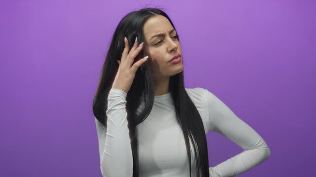 Woman pondering over isolated purple background wearing white shirt showing thoughtful expression.