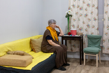 Elderly woman sitting on sofa and looking away. Home care and social assistance for older adults. Senior citizen support and loneliness concept