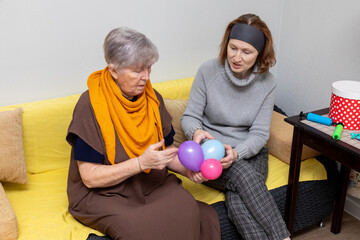 Social worker woman helping senior woman play with balloons. Elderly care and assistance. Concept of support and companionship for older people