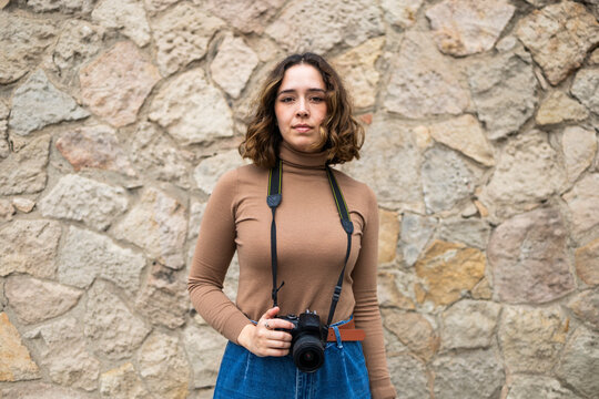 Woman with camera standing against stone wall background