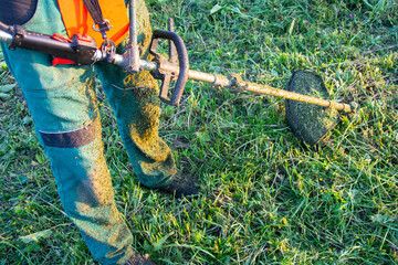 Worker Cutting Grass with Brush Cutter at Sunset