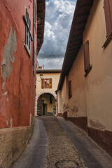 Obraz premium A picturesque narrow alley with colorful warm-toned walls, an arched passage, and dramatic clouds in a traditional Italian village.