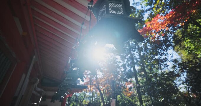 Beautiful old metal lamps hanging from ancient Japanese roof with sun shining through autumn trees