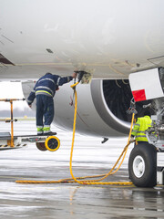 Airport ground crew workers connecting external power supply cable to a commercial airplane