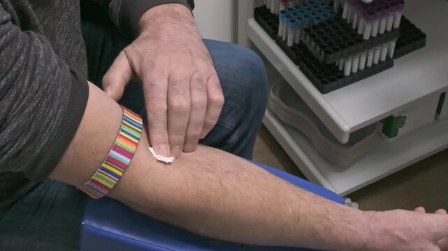 Gloved hands removing needle and patient pressing cotton pad firmly on the inside of the elbow.