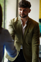 Man extends hand to shake with another person in a bright indoor space during a meeting or conversation at an unspecified time
