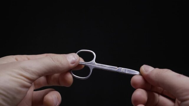 A person's hands hold and examine a small pair of metal nail scissors, opening and closing the blades. Concept of personal grooming, hygiene, self-care, and using precise tools.
