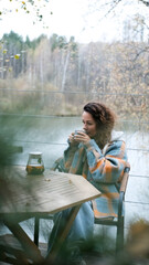 A sweet woman with curly hair drinks tea and relaxes on the terrace of her house on an autumn day. Health care, sincerity, a sense of balance and calm.