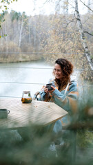 A sweet woman with curly hair drinks tea and relaxes on the terrace of her house on an autumn day. Health care, sincerity, a sense of balance and calm.