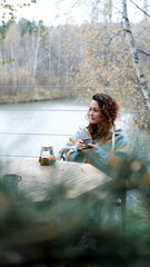 A sweet woman with curly hair drinks tea and relaxes on the terrace of her house on an autumn day. Health care, sincerity, a sense of balance and calm.