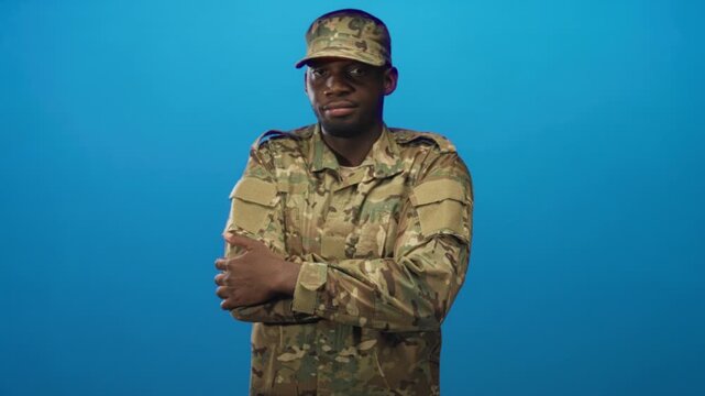 Soldier man in camouflage uniform and cap with arms crossed showing hands in studio; duty resilience.