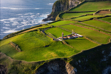 Cintrao headland on lighthouse above bright green fields on the north coast of Sao Miguel, Azores, Aerial view
