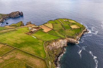 Agricultural countryside on dramatic green cliffs above Atlantic Ocean in Azores. Coastal island scenery, aerial view