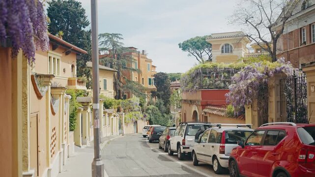 A small street with houses cover in beautiful foliage has cars parked in a row. Rome, Italy.