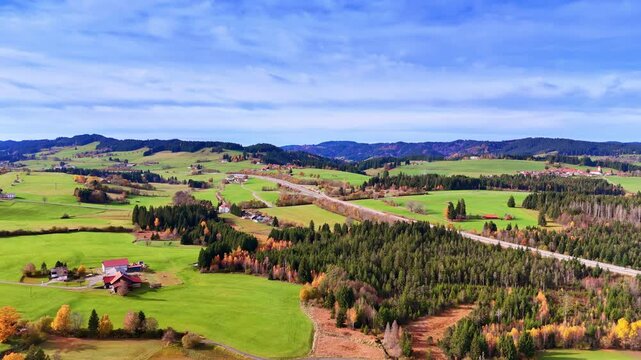 Highway crossing rural Bavarian landscape with green fields. Aerial perspective of a road through farmland and forests with small villages and mountains.