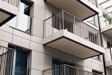 Fototapeta premium Modern apartment building balconies. White facade with metal railings. Residential block exterior detail. New housing building in city. Urban apartment architecture with repeating balcony structure.