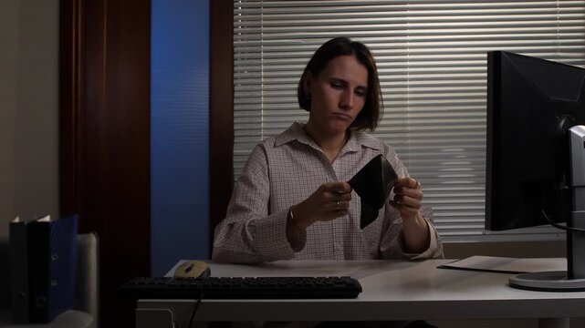 Woman looking disappointed and anxious, holding an empty wallet at her office desk, facing financial difficulties, debt, and economic crisis, feeling worried about money problems