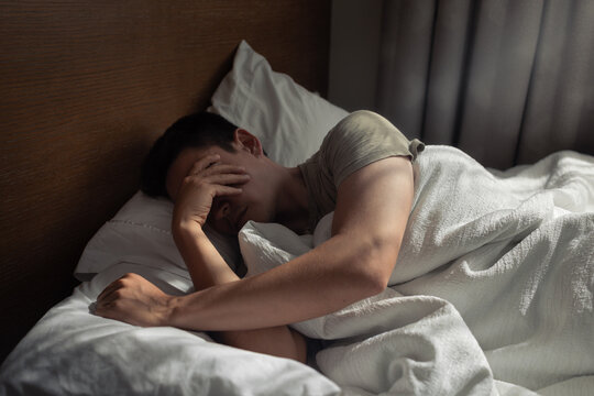 Exhausted Man Covering Face in Bed &ndash; Anxiety, Burnout and Sleepless Night

