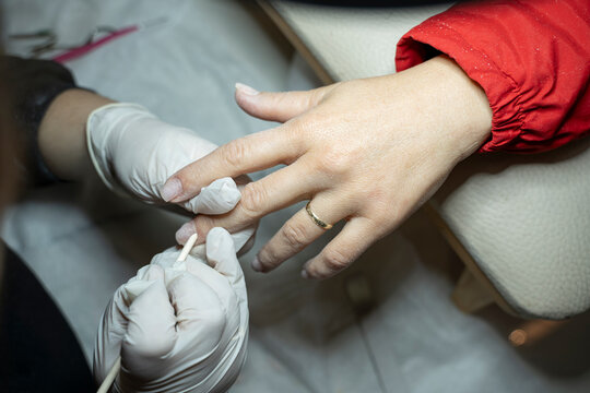 In a beauty salon, a manicurist pushes back a client's cuticles with a wooden tool (Stock Photo).