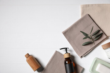 Towels, cosmetic products and green leaves on white wooden table, flat lay. Space for text
