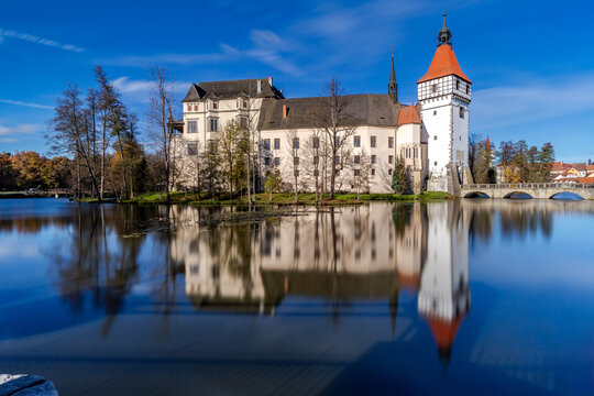 Autumn at Blatn&aacute; Castle in South Bohemia - the castle and the blue sky are reflected on the surface of the pond