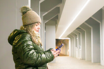 Woman wearing a green anorak and hat on the street holding a smartphone
