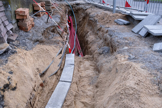 Excavation trench with red utility cables and bricks. construction excavation area along the road