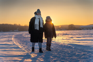 Mother and Daughter Walking on Snowy Path Across Frozen Lake at Sunset, Winter Family Love