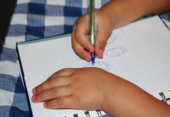 Small child's hand drawing blue scribbles on a notebook